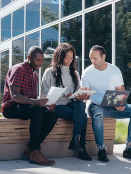 A group of diverse colleagues brainstorming outdoors with documents and a laptop.