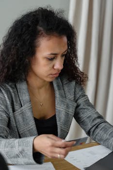 A professional woman analyzing financial documents at her office desk using a laptop.